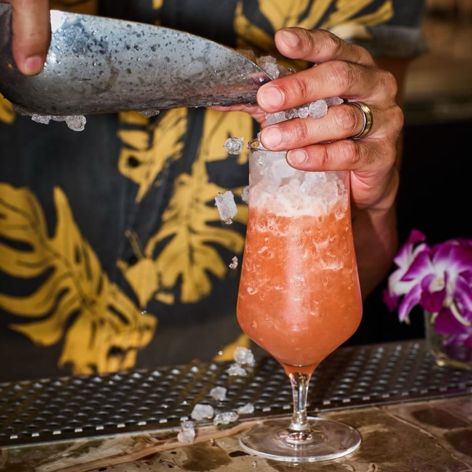 Bartender in a Hawaiian shirt adding crushed ice to a vibrant red cocktail at Edgemar Restaurant.