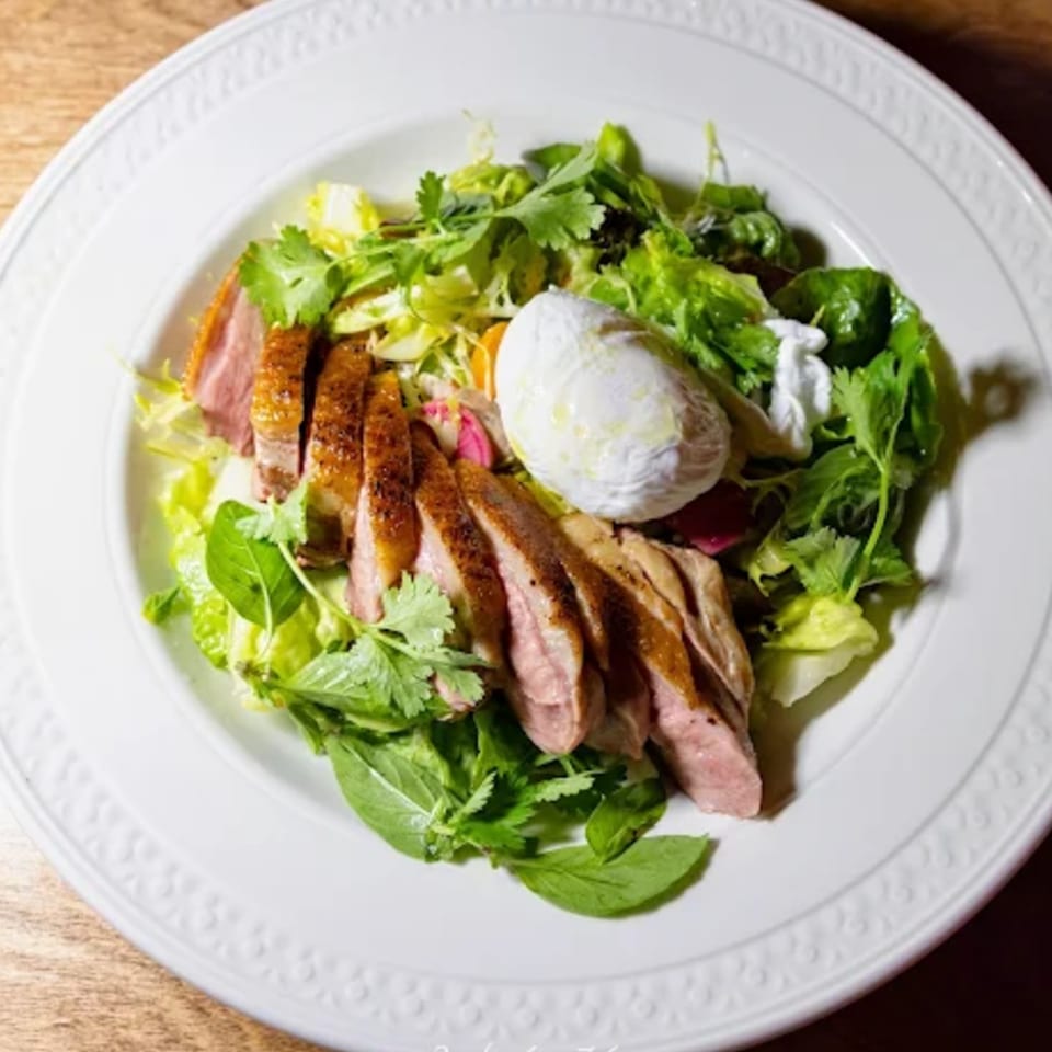 Sliced duck breast with a poached egg and fresh greens on a white plate at Edgemar Restaurant.