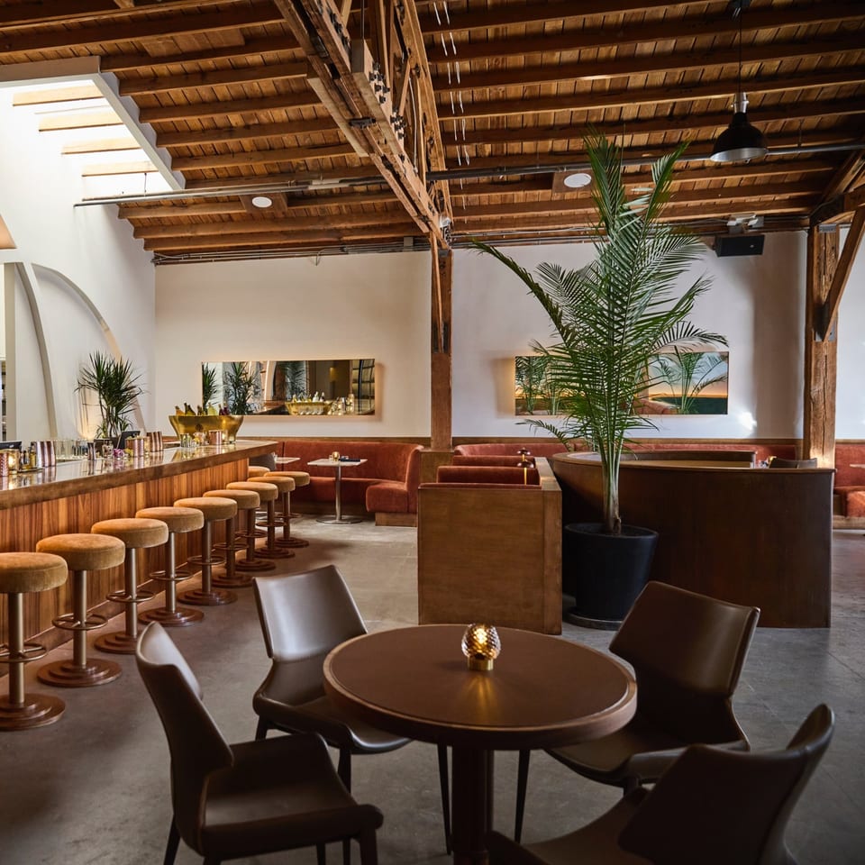 Edgemar Restaurant + Lounge interior with a long bar, velvet stools, and cozy seating areas.