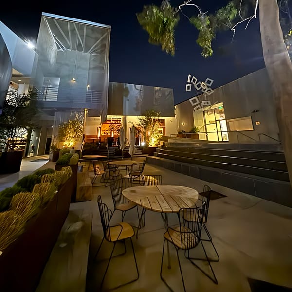 Edgemar Restaurant + Lounge's outdoor patio at night, with modern tables, chairs, and illuminated architecture.