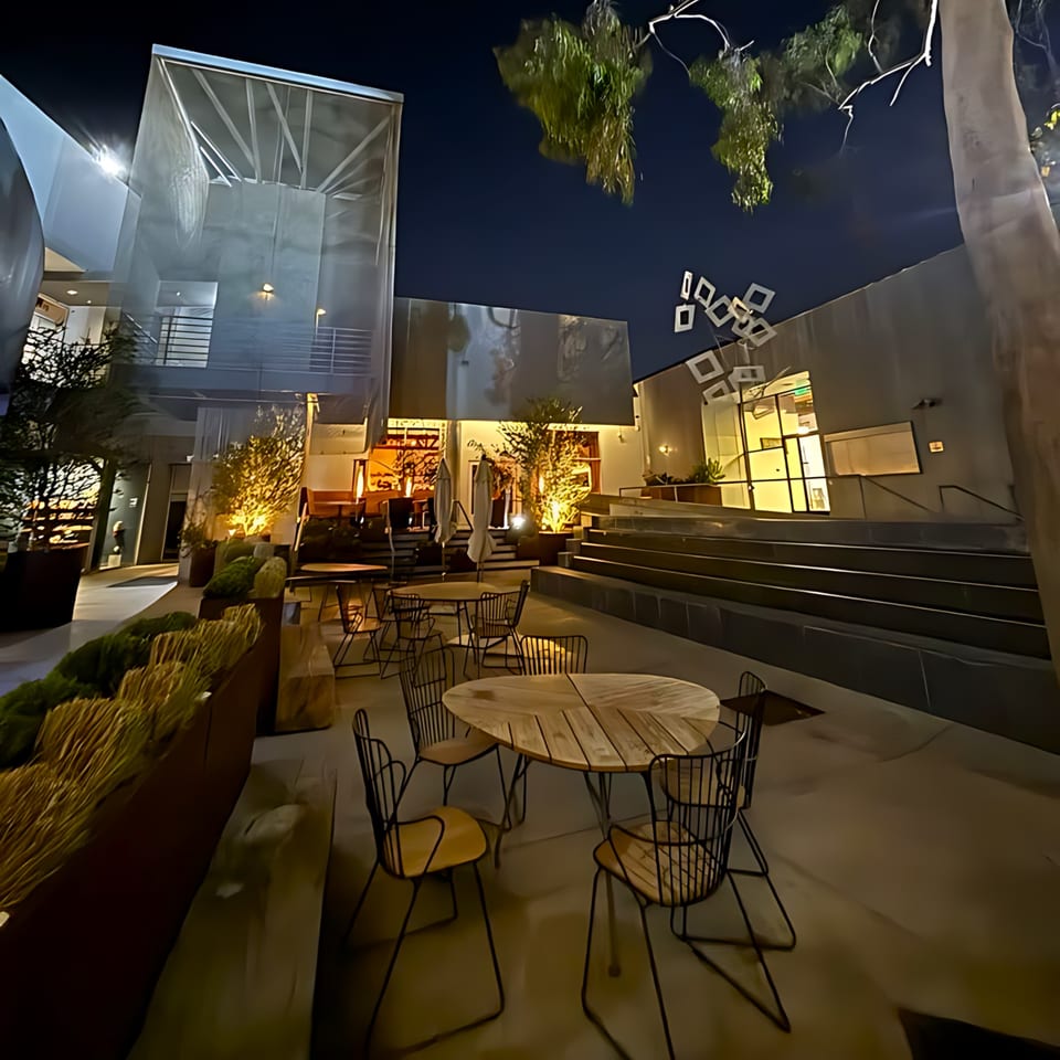 Edgemar Restaurant + Lounge's outdoor patio at night, with modern tables, chairs, and illuminated architecture.
