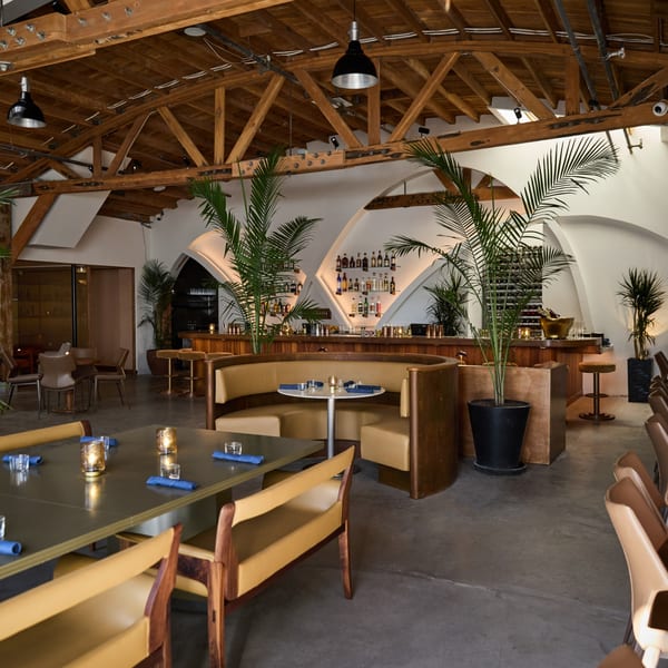 Edgemar Restaurant + Lounge interior with a bar, wooden ceiling, and tan seating with blue napkins.