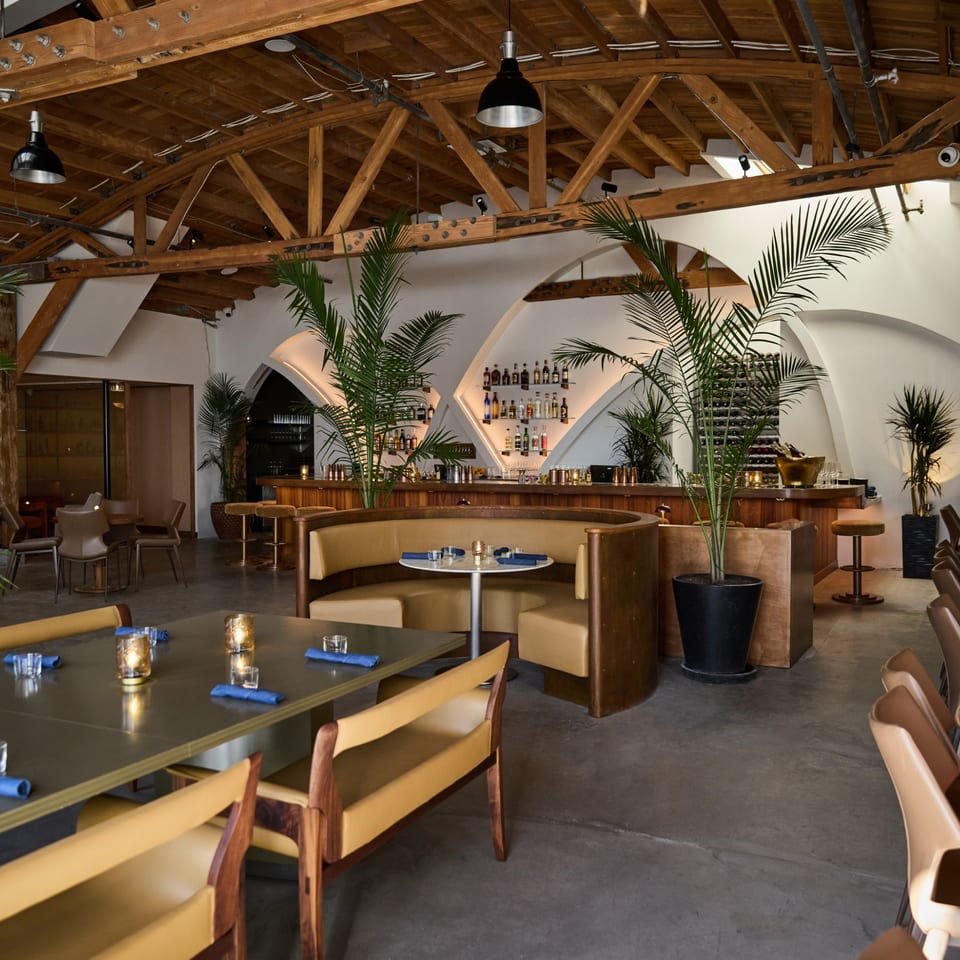 Edgemar Restaurant + Lounge interior with a bar, wooden ceiling, and tan seating with blue napkins.