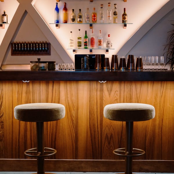 A modern Edgemar Restaurant + Lounge bar with two stools, liquor bottles, and beer taps.