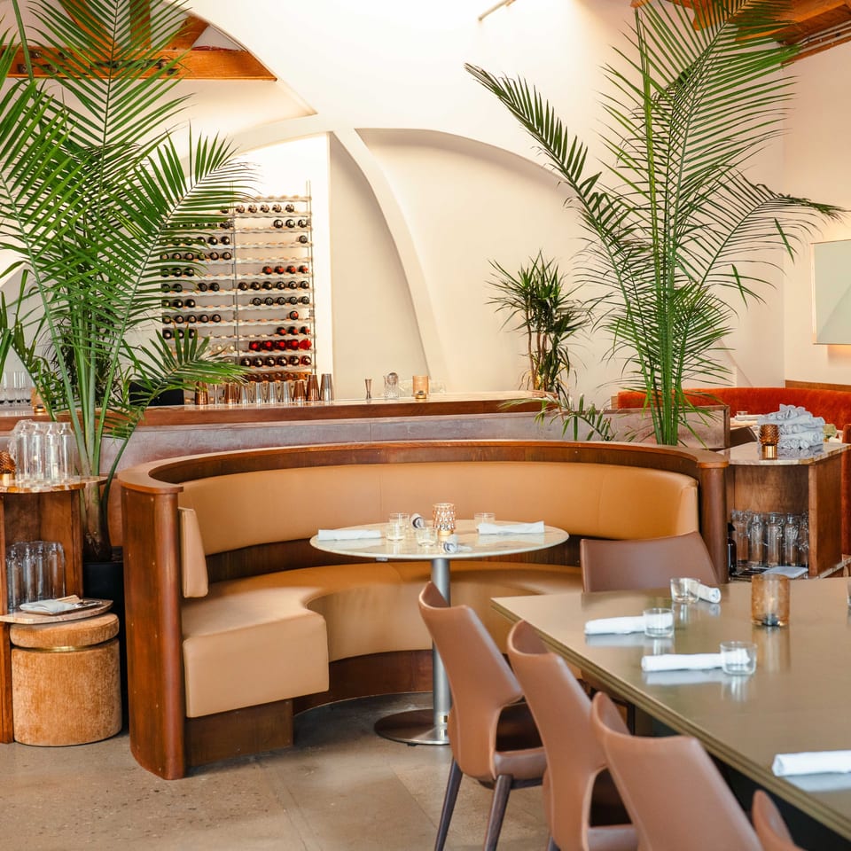 Edgemar Restaurant's dining area with curved tan booths, tables, potted palms, and a wine rack.