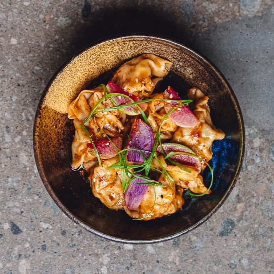 Edgemar Restaurant + Lounge's dumplings with purple radish slices and green herbs in a dark bowl.