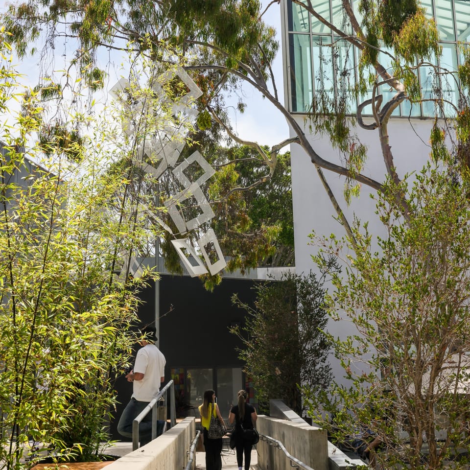 Guests walk up a ramp towards the Edgemar Restaurant + Lounge entrance, surrounded by lush greenery and modern architecture.