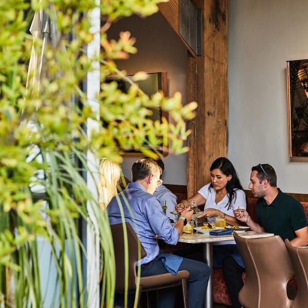 Diners enjoying New American cuisine at Edgemar Restaurant + Lounge, seen through lush green foliage.