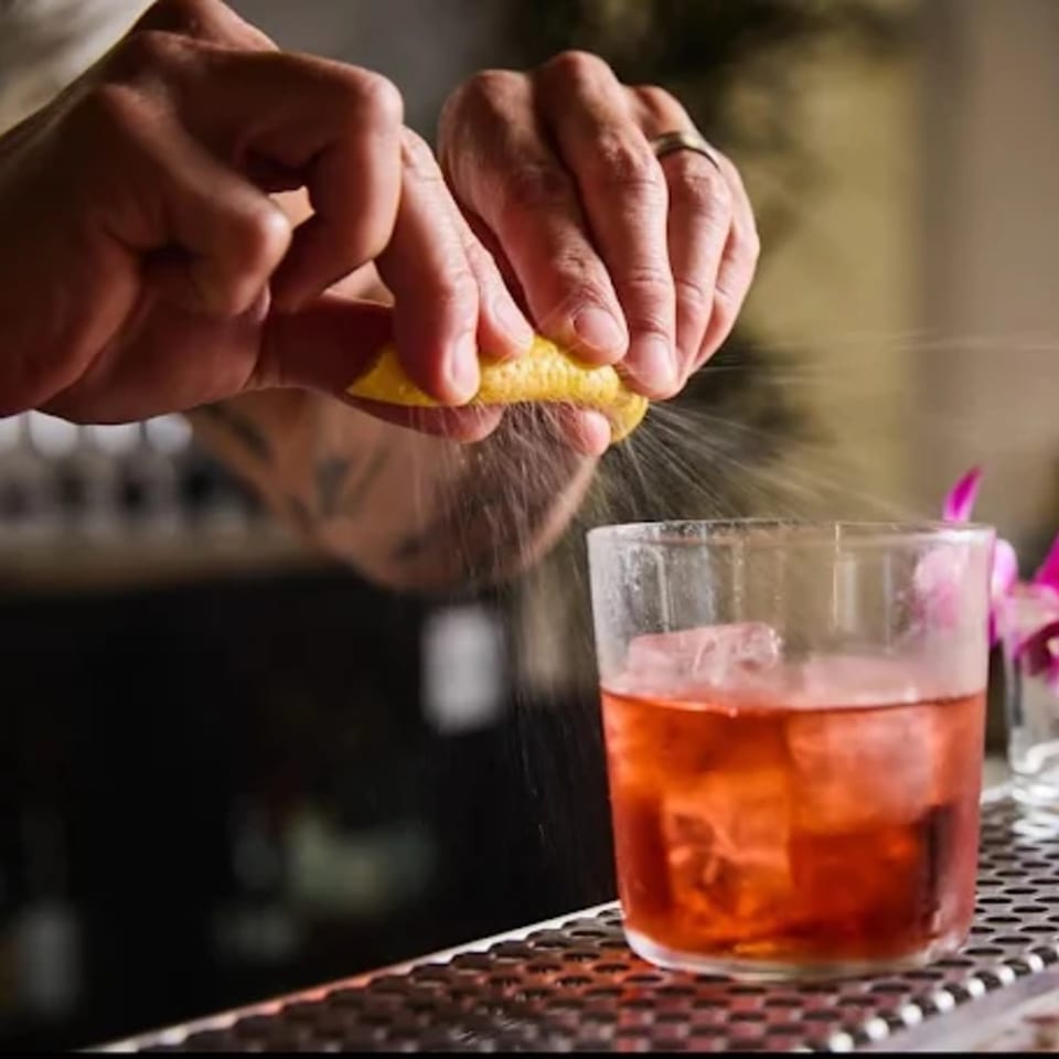 Bartender squeezing a lemon peel over a red cocktail with ice at Edgemar Restaurant + Lounge.