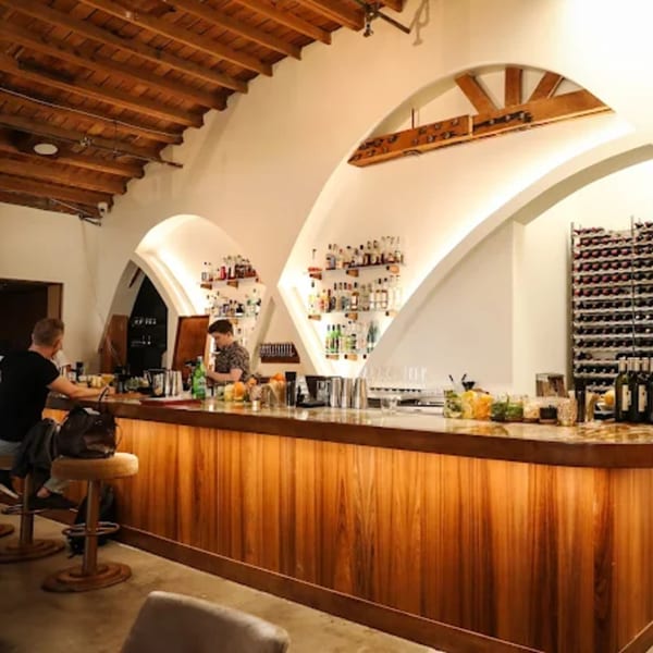 Edgemar Restaurant + Lounge bar with a bartender, customer, and wine rack under arched ceilings.