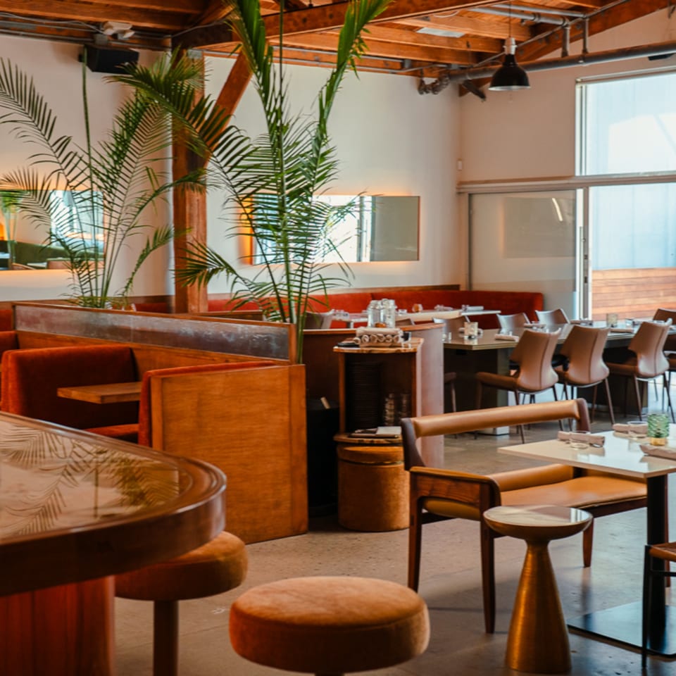 Edgemar Restaurant + Lounge interior with modern wooden and red velvet seating, lush plants, and exposed beams.